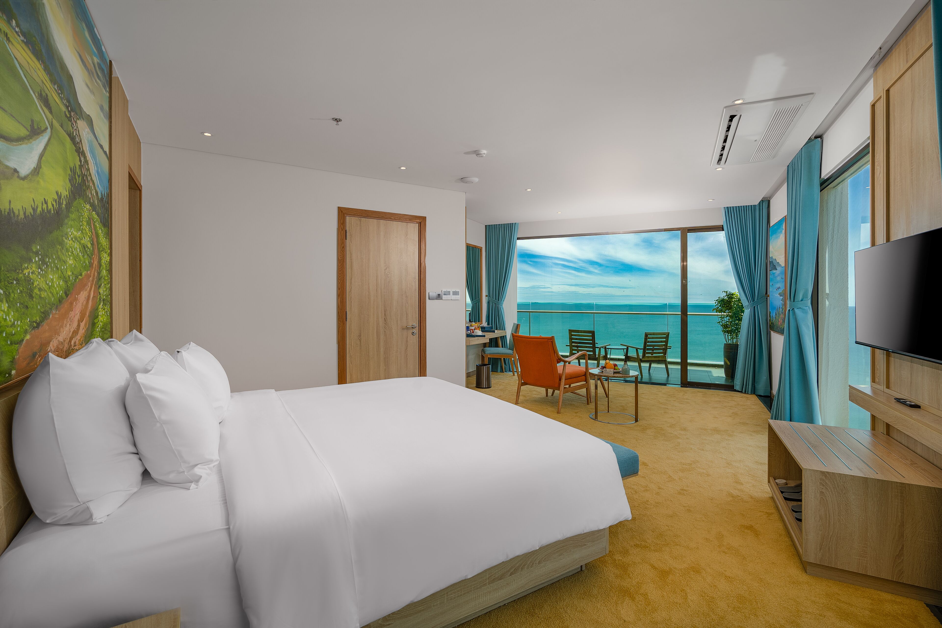 Habitación de hotel con una cama grande, un escritorio, una silla, un televisor y un balcón con vista al mar.