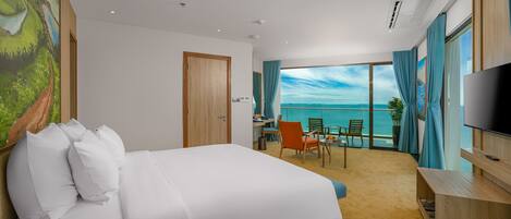 Habitación de hotel con una cama grande, un escritorio, una silla, un televisor y un balcón con vista al mar.