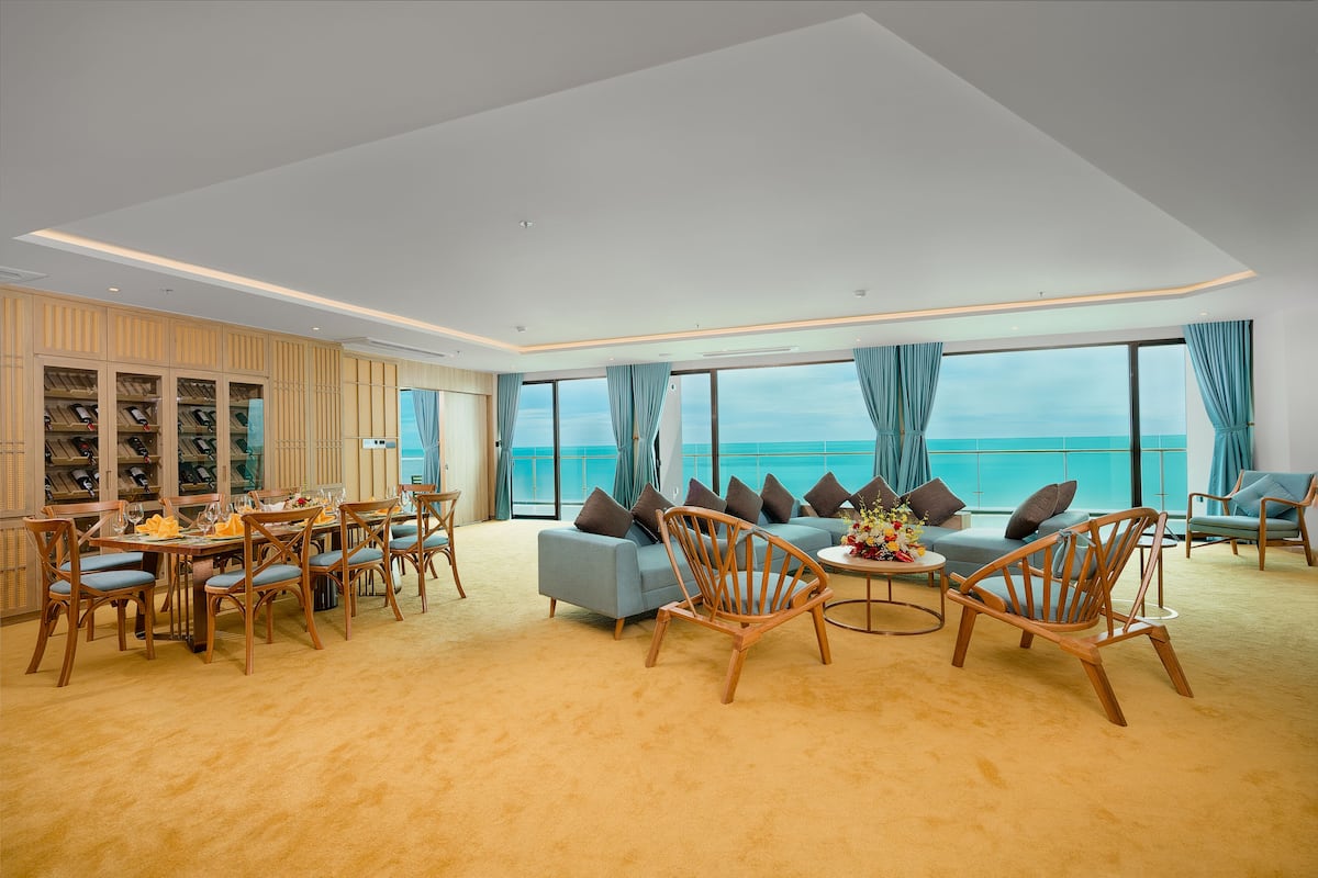 Ein geräumiges Wohnzimmer mit einer großen Couch, Holzstühlen, einem Esstisch und Meerblick.