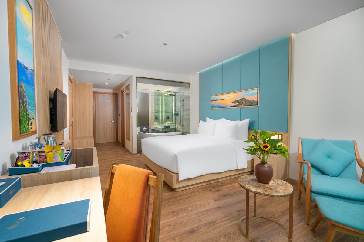Ein Hotelzimmer mit Bett, Schreibtisch, Stuhl, kleinem Tisch mit Blumenvase und einem Bild an der Wand.