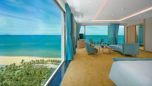 Une chambre d’hôtel moderne dotée d’une grande fenêtre donnant sur une plage, d’un canapé, d’une petite table et d’un lit.