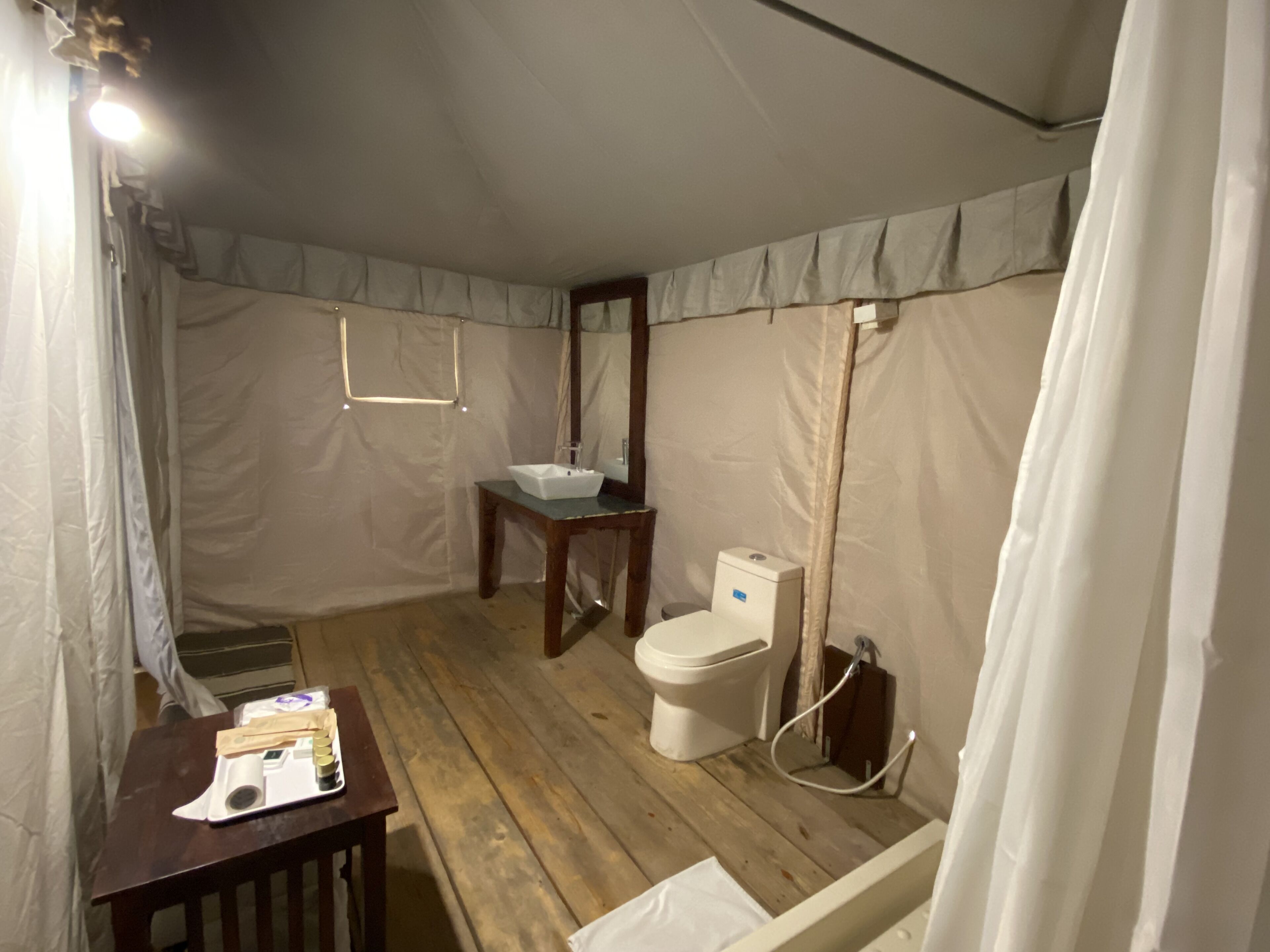 A small, compact bathroom with a wooden floor, a white sink, a toilet, and a mirror.