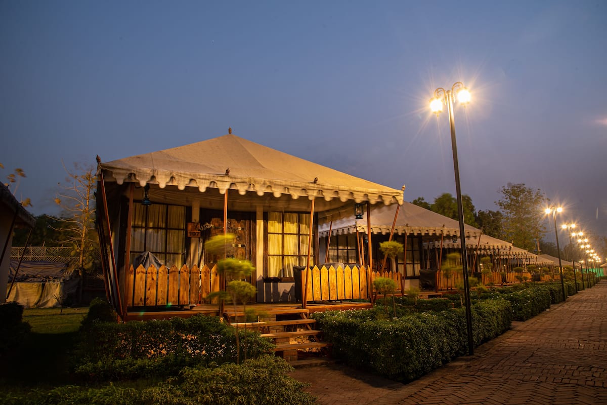 A tented structure with a wooden fence, steps leading up to the entrance, and a paved pathway.