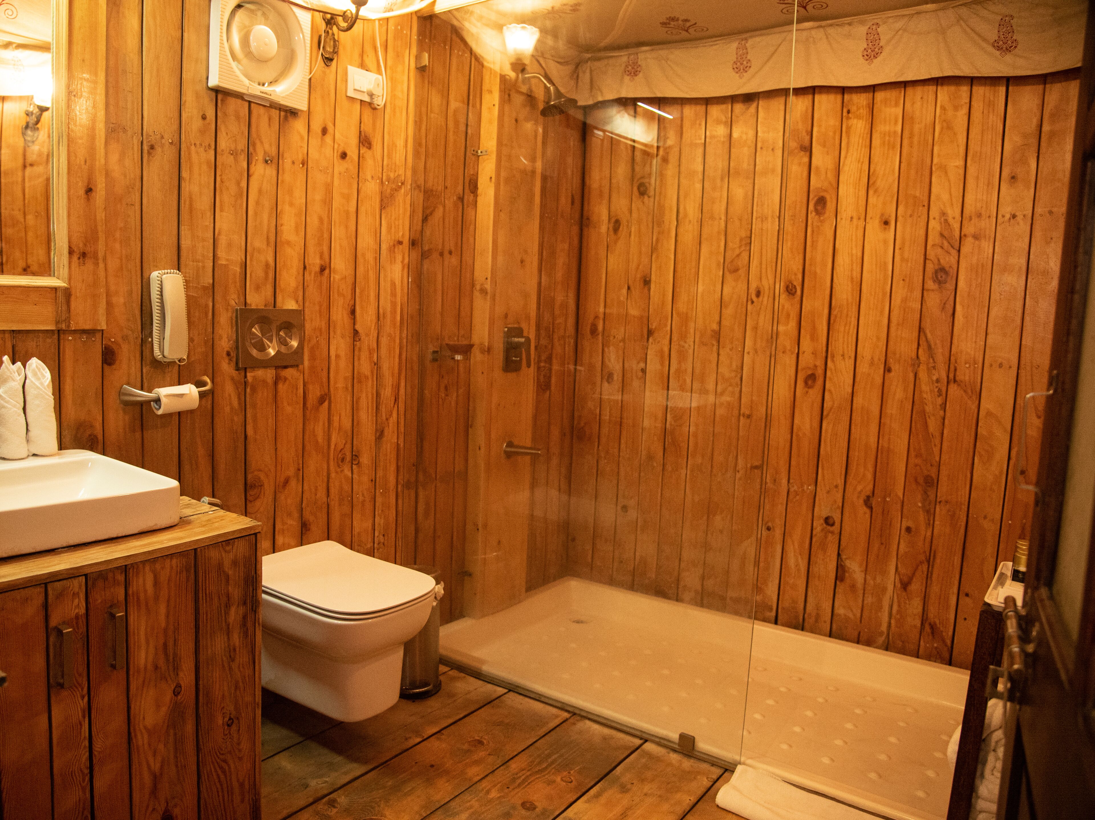 A wooden bathroom with a toilet, sink, and shower.