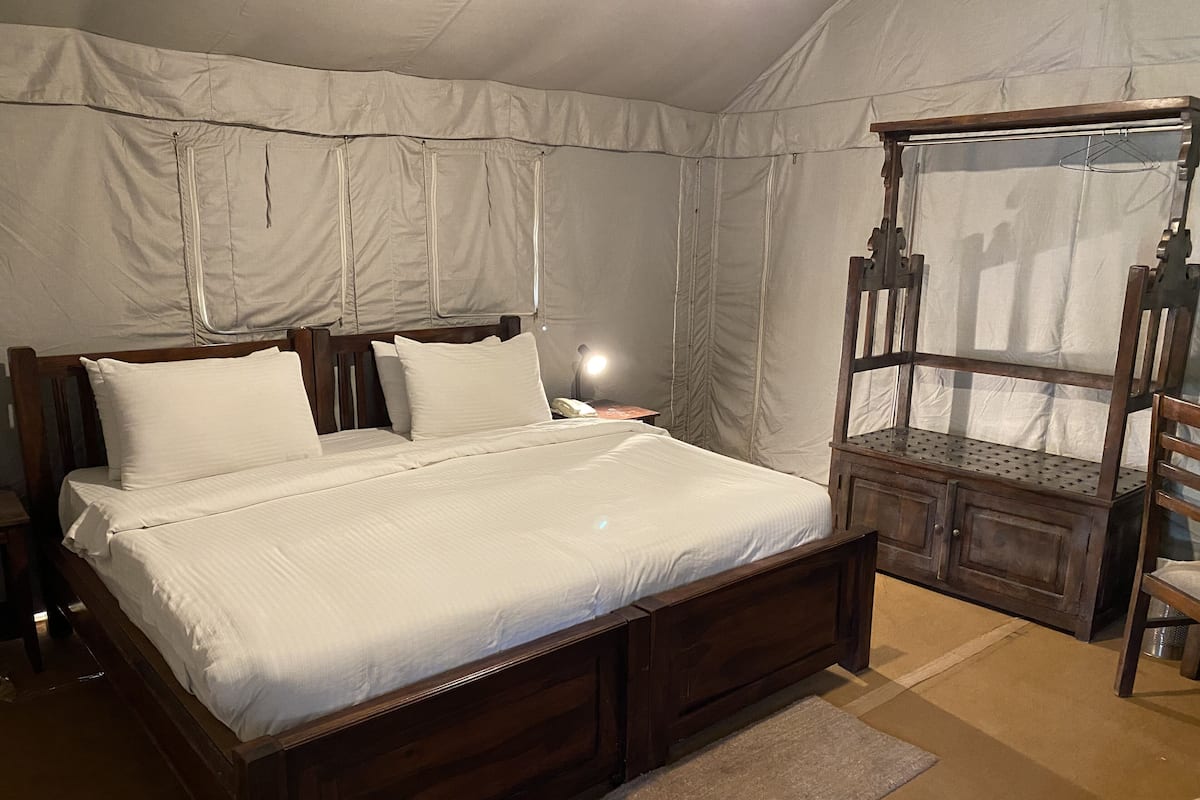A bedroom with a wooden bed, white bedding, a nightstand, a hanging chair, and a tent-like structure in the background.