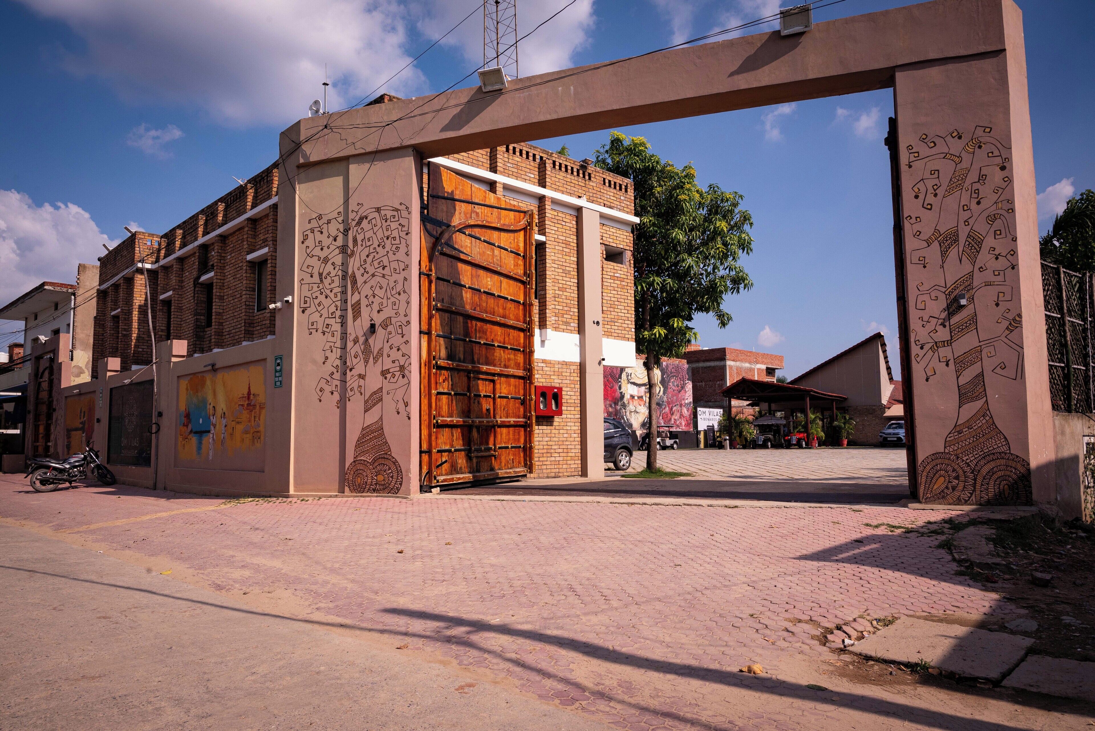A building entrance with a large wooden gate, brick walls, and a mural on the side.