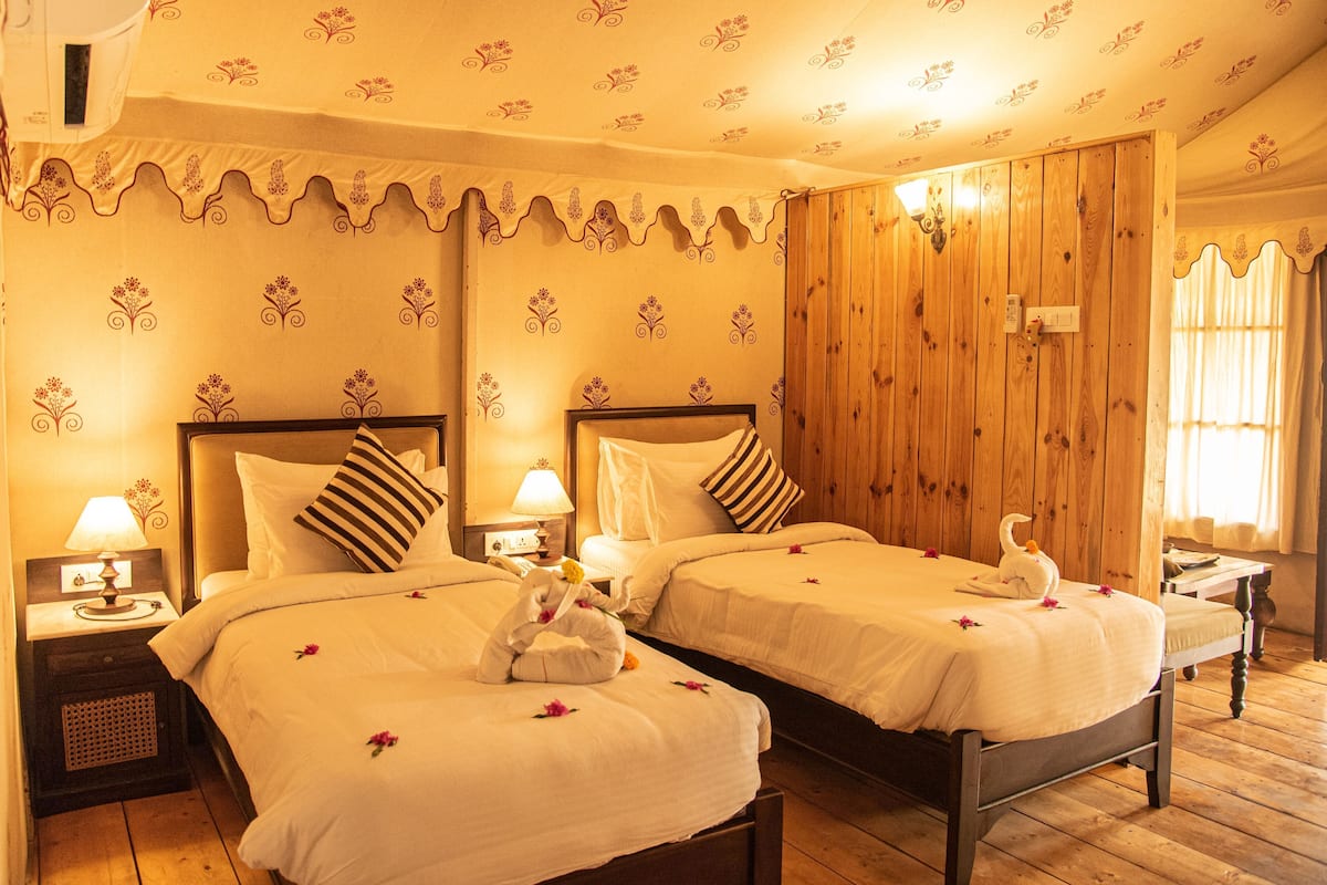 A hotel room with two beds, wooden paneling, floral wallpaper, and a wooden floor.