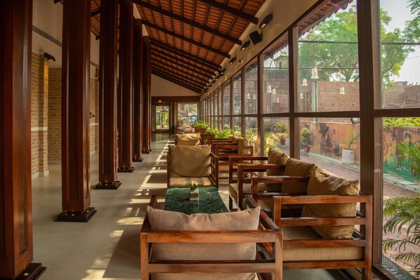 A corridor with wooden benches and tables, large windows, and a brick wall. - Om Vilas Benares, Varanasi (Varanasi)