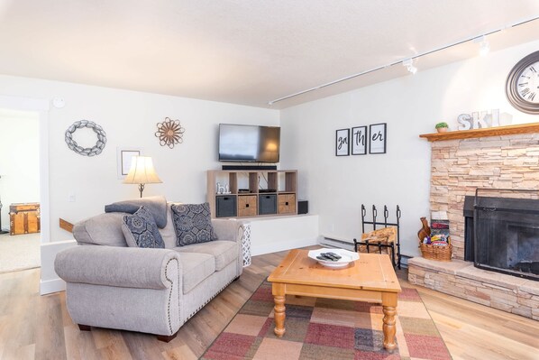 A living room with a sofa, coffee table, TV, fireplace, and stone wall.