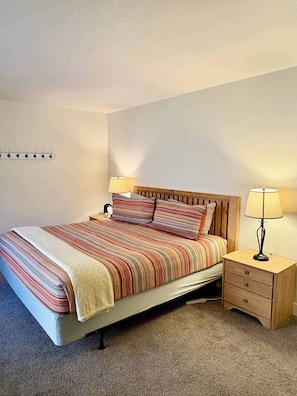 A neatly made bed with striped bedding, two bedside tables with lamps, and a wall-mounted light switch.