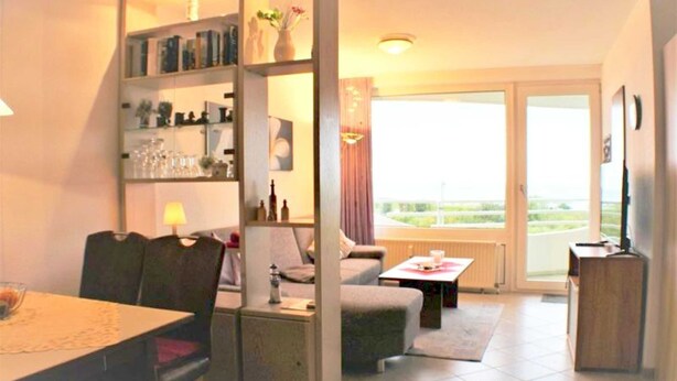 Un salon comprenant un canapé, une table basse, une table à manger avec des chaises, une bibliothèque et un téléviseur.