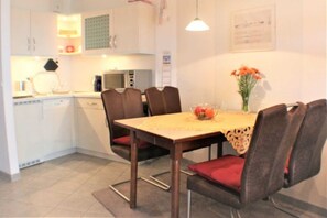 Cocina compacta con armarios blancos, un microondas y una mesa de comedor con cuatro sillas.