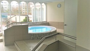 Une piscine intérieure moderne, dotée d’un sol carrelé et d’une paroi en verre, située à côté d’un escalier menant à un deuxième étage.