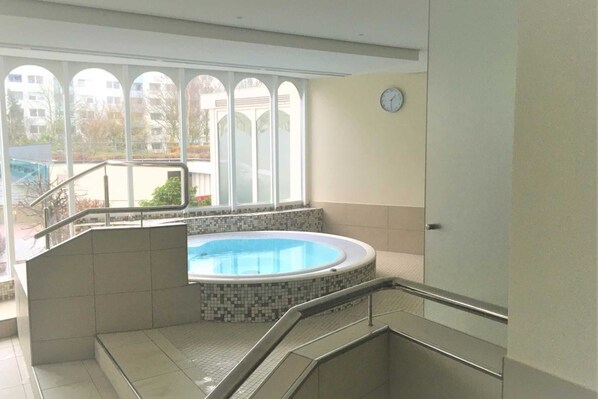 A modern indoor swimming pool with a tiled floor and a glass enclosure, adjacent to a staircase leading to a second floor.