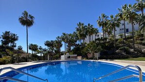 A clear blue swimming pool surrounded by palm trees and a white building. - Oasis de Capistrano Rabat 27 by Casasol (Nerja)