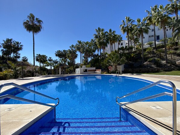 Una piscina azul cristalina rodeada de palmeras y un edificio blanco.