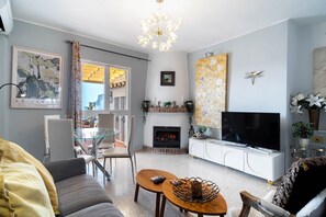 Un salon avec une cheminée, un téléviseur et un coin repas comprenant des chaises et une table en verre.