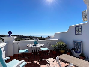 Une terrasse avec une table et des chaises, des plantes en pot et une vue sur la mer.