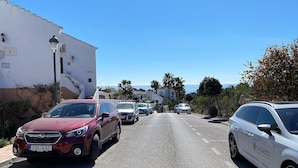 A street lined with parked cars and buildings, leading towards a coastal view. - Oasis de Capistrano Rabat 27 by Casasol (Nerja)