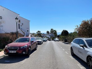 Calle bordeada de coches aparcados y edificios, que se abre a una vista costera.