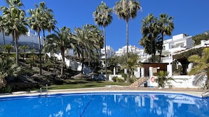 A clear blue pool surrounded by palm trees and white buildings. - Oasis de Capistrano Rabat 27 by Casasol (Nerja)