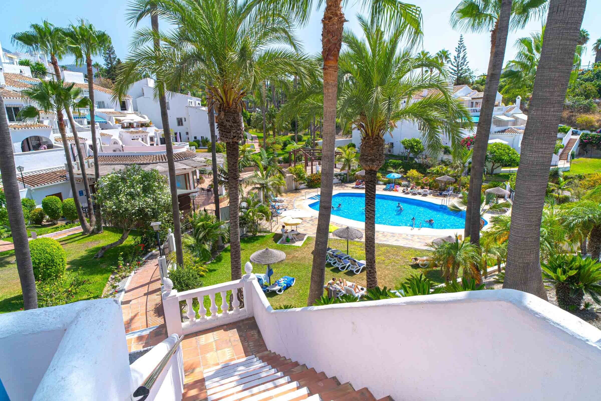 Un resort con piscina rodeada de palmeras y edificios blancos.