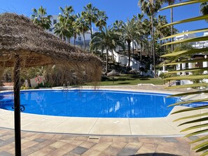 Una piscina azul cristalina rodeada de palmeras y una estructura de techo de paja.