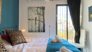 A bedroom with a bed, a window with curtains, a wall-mounted air conditioner, and a painting of trees. - Oasis de Capistrano Rabat 27 by Casasol (Nerja)