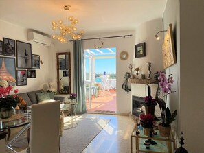 A spacious living room with a large window, a chandelier, and various decorative items.