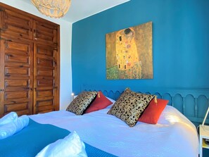 A bedroom with a large bed, a wooden wardrobe, and a painting of a castle on the wall.