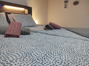 A neatly made bed with patterned bedding, a headboard with integrated lighting, and a wall-mounted light fixture. - Apartment Iskra (Plitvicka Jezera)