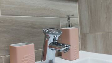 Uma pia de banheiro com torneira cromada, dois dosadores de sabonete rosa e um espelho acima.