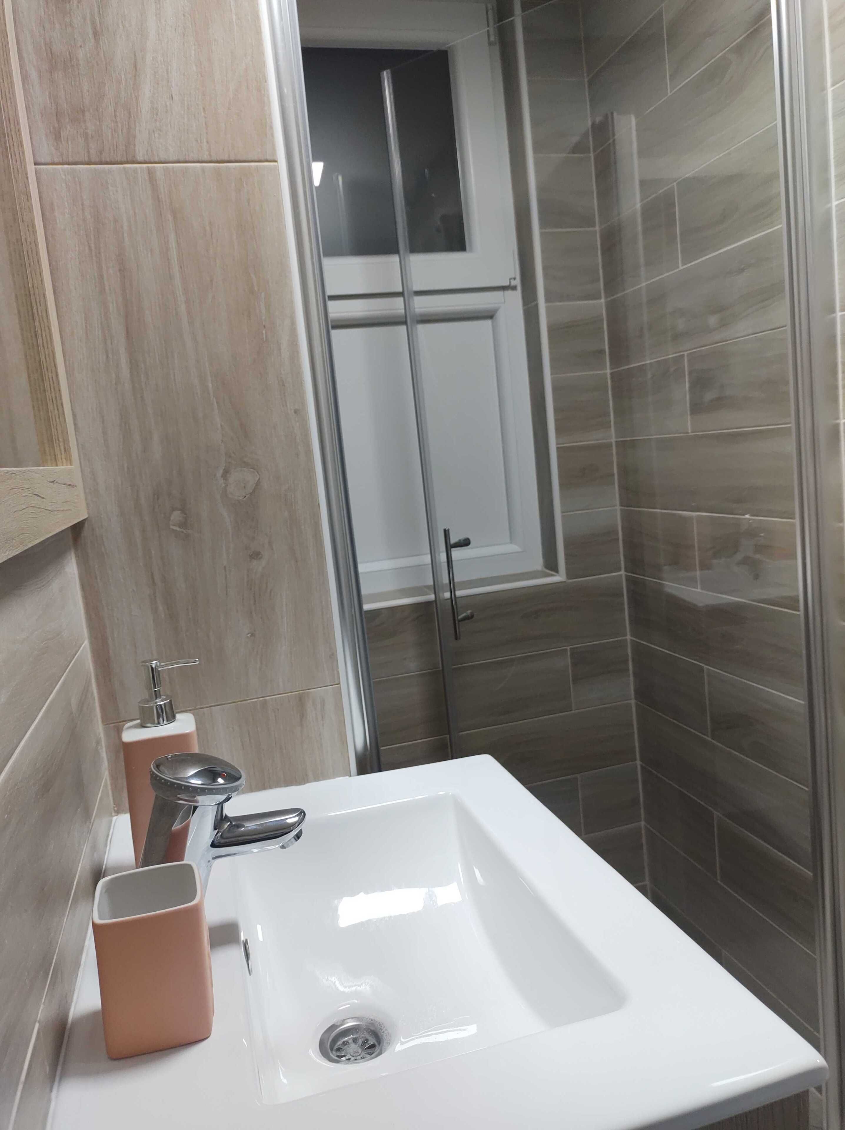 Un baño con lavamanos blanco, dispensador de jabón y cabina de ducha de vidrio.