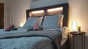 A modern bedroom with a bed, patterned bedding, a bedside table with a lamp, and a decorative wall piece. - Apartment Iskra (Plitvicka Jezera)