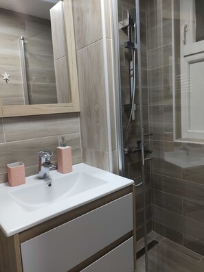 A bathroom with a white sink, two pink soap dispensers, a mirror, and a glass-enclosed shower area. - Apartment Iskra (Plitvicka Jezera)