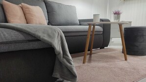 A modern living room with a grey sofa, a small wooden side table, and a pink rug. - Apartment Iskra (Plitvicka Jezera)