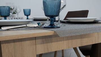 A dining table with a laptop, blue glassware, and a wooden wall clock.