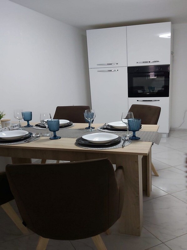 A dining area with a wooden table set for four, equipped with plates, glasses, and cutlery. - Apartment Iskra (Plitvicka Jezera)