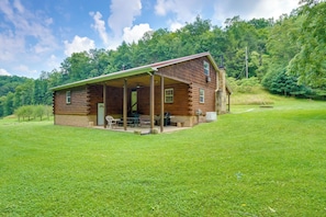 Situated in a lush landscape, this cabin features a covered porch and a simple design with a chimney.