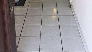 Un pasillo con piso de baldosas, una puerta de madera al final y un felpudo con la palabra 'HOME'.