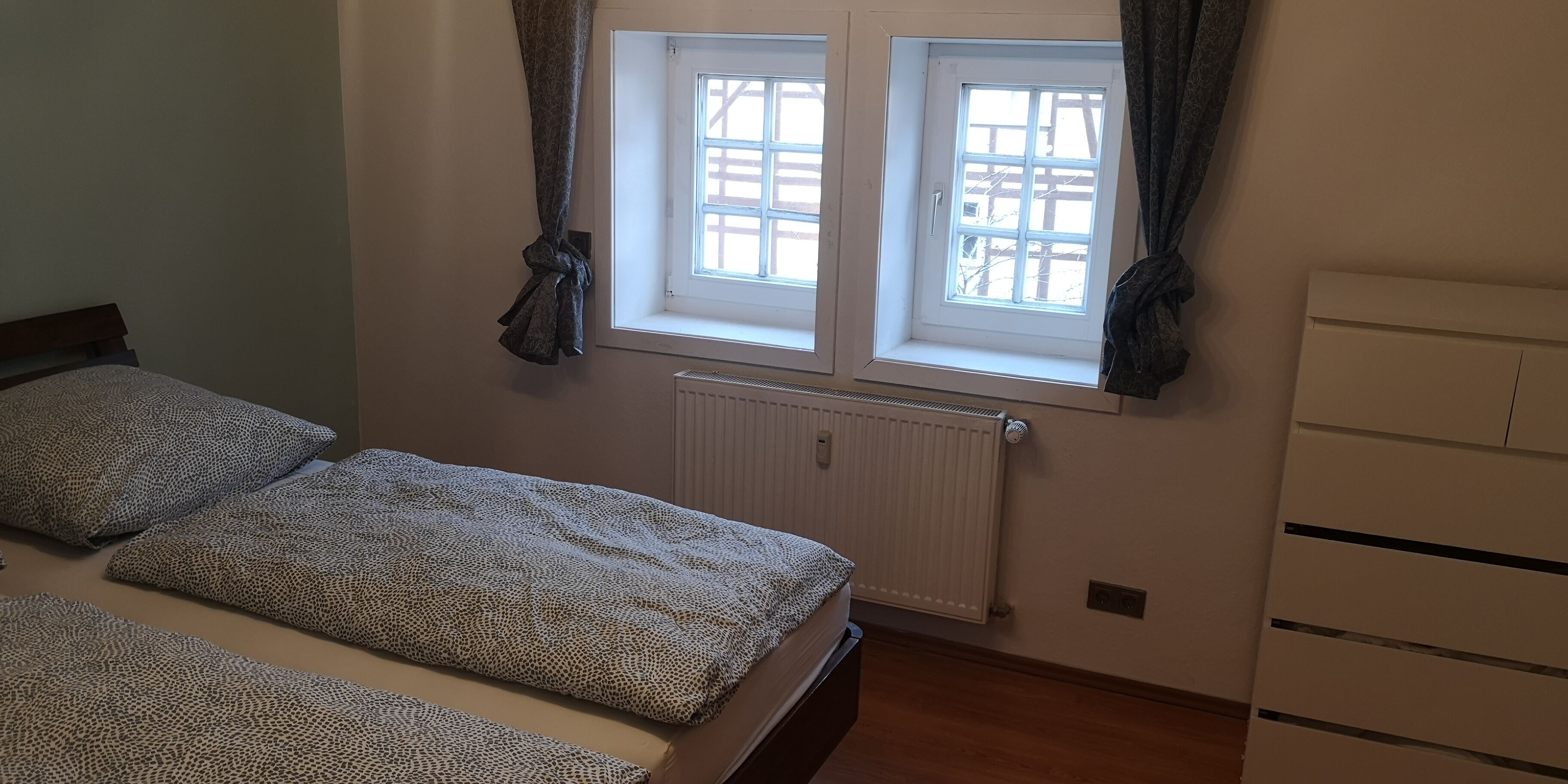 A bedroom with a bed, a radiator, and a window with curtains.