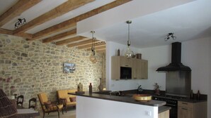 A kitchen with a stone wall, wooden beams, a large island, and a built-in stove. - Le clos des oiseaux is a winery located in Aimargues. (Aimargues)