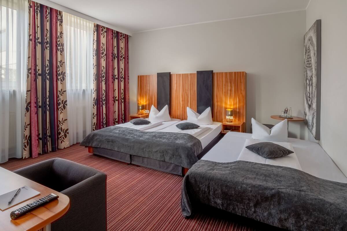 A hotel room with two beds, a desk with a chair, a small table, and a large painting on the wall.