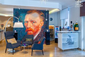 Un vestíbulo moderno con un cuadro abstracto grande, asientos cómodos, una recepción y una minibar.