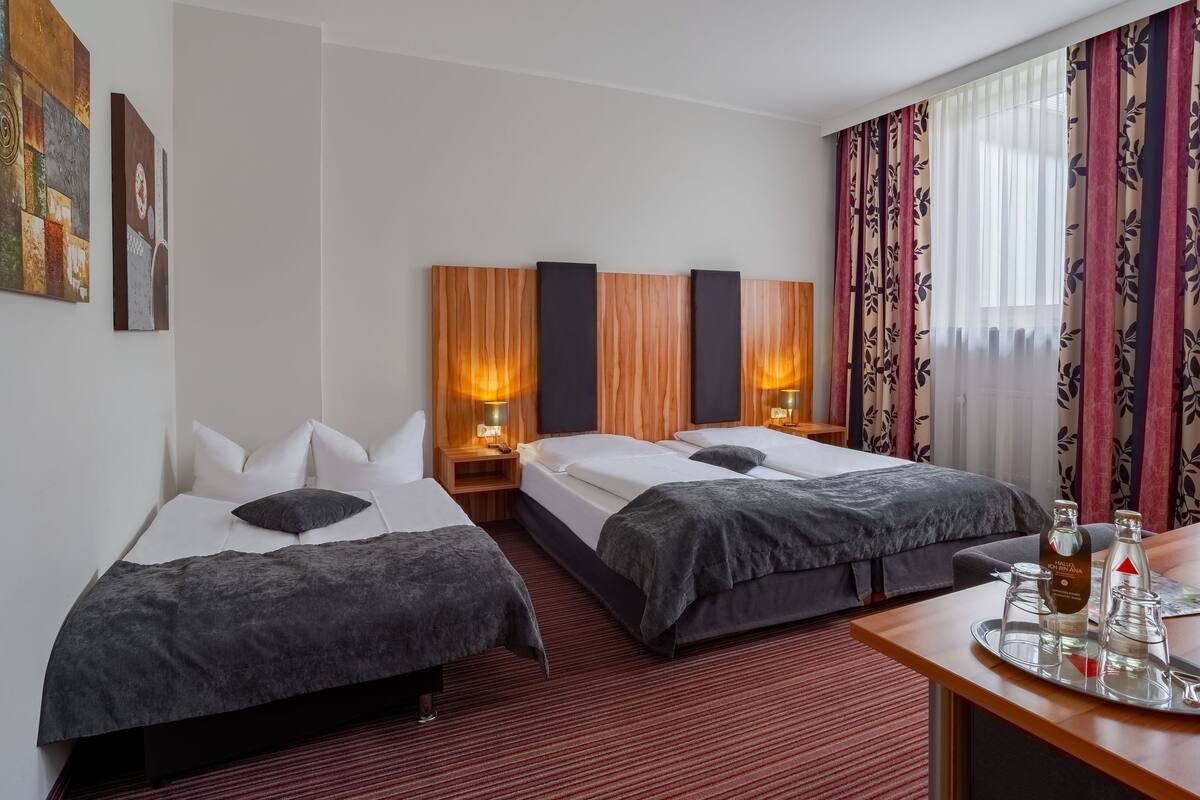 A hotel room with two beds, a desk with a tray, and a large window with curtains.