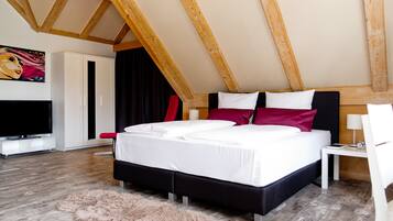 A bedroom with a large bed, wooden ceiling beams, a TV, and a fluffy rug.