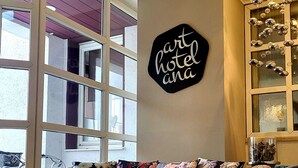 A room with a sofa, a decorative sign, a window, and a chandelier. - Arthotel ANA Style (Augsburg)