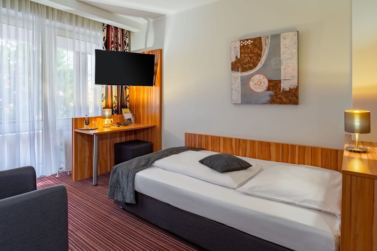 A hotel room with a bed, a desk, a chair, a TV, and a painting on the wall.