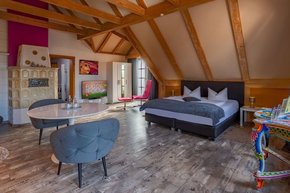 A cozy attic bedroom with a large bed, a dining table, and a kitchen area.