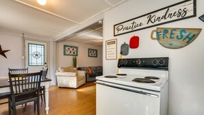 Una cocina con estufa blanca, sillas de madera, una mesa de comedor y una isla de cocina. Hay adornos en la pared, incluyendo un letrero que dice "Practice Kindness" y otro con la palabra "FRESH".